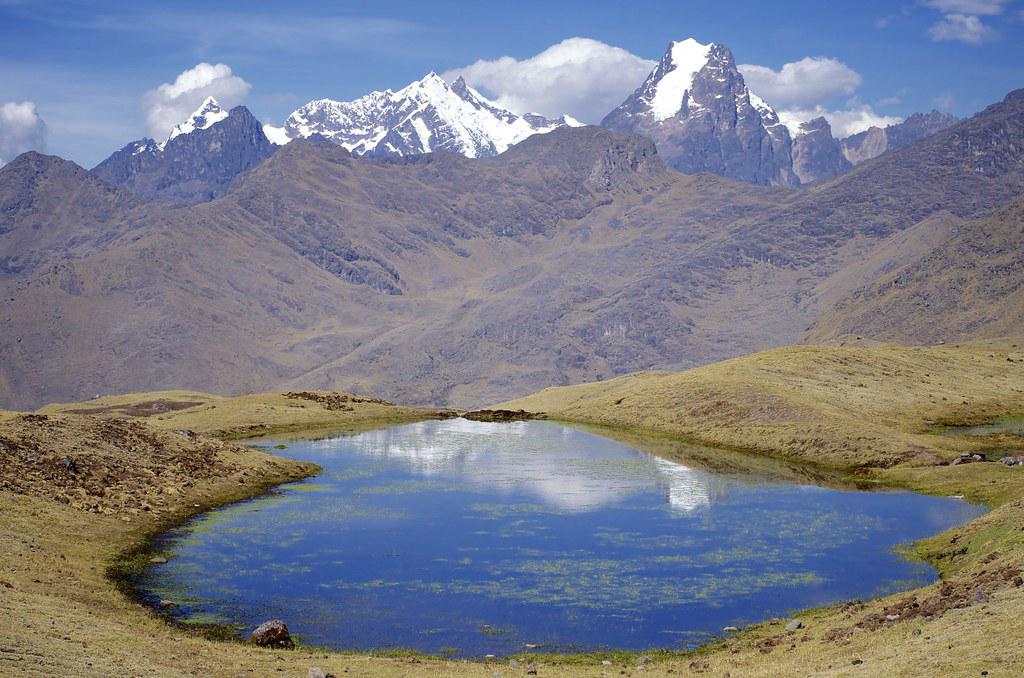 A panoramic view of towering Andean mountain peaks with a river and greenery