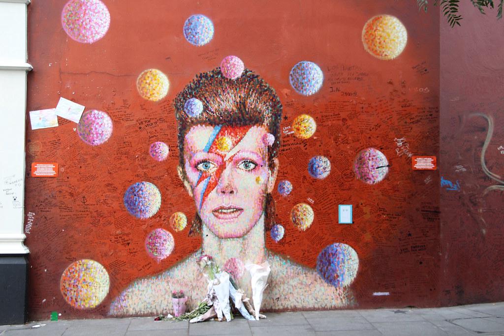 The iconic David Bowie mural in Brixton, featuring a stunning portrait of the late artist in vibrant colours and textures, surrounded by tributes from fans.