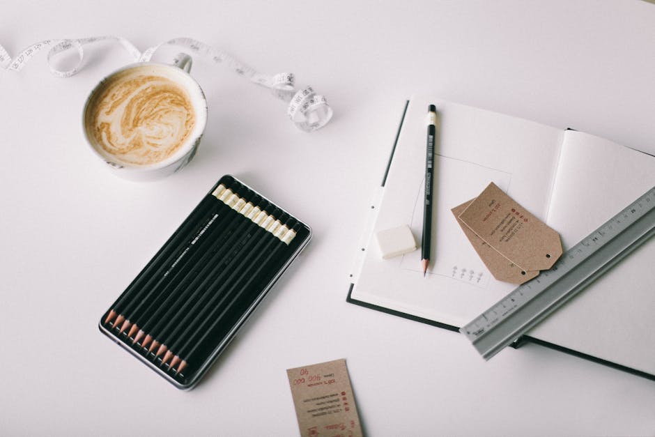 A close-up of drawing supplies including a ruler, pencil, and eraser on a table with a sketchbook open to a page with a grid drawn on it.